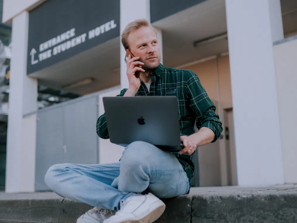 Mann mit Laptop sitz vor Eingang