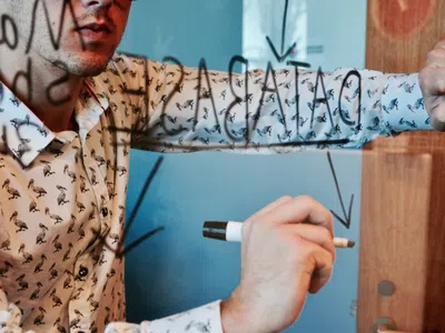 Mann im Hemd schreibt mit schwarzem Filsstift auf Whiteboard