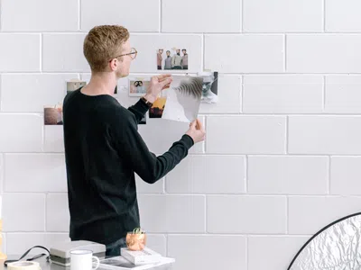 Ein Mann hält ein Blatt Papier vor einer weißen Ziegelwand.