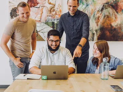 Eine Gruppe geprüfter Wirtschaftsfachwirte (IHK) steht mit Laptops um einen Tisch.