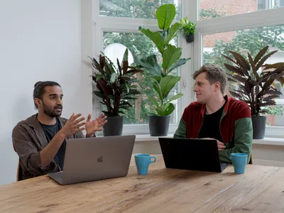 Zwei IT-Manager sitzen mit Laptops an einem Tisch.