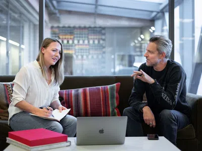 Ein leitender Manager und ein Praktikant sitzen mit einem Laptop auf einer Couch.