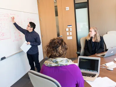 Eine Gruppe von Spezialisten für Wirtschaftsinformatik sitzt mit Laptops an einem Tisch.