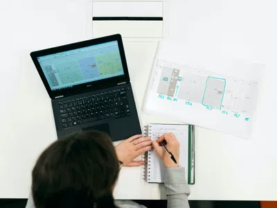 Techniker: in der Konzeptentwicklung, der an einem Schreibtisch auf ein Notizbuch schreibt.