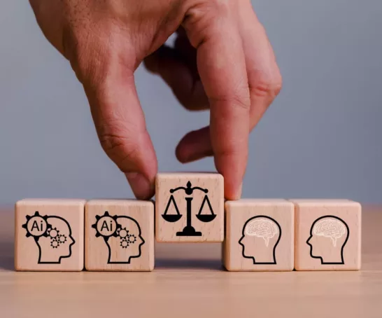 and setzt einen Holzklotz mit einer Waage zwischen Klötze mit KI- und Gehirn-Symbolen – Darstellung der Balance zwischen Technologie, Ethik und menschlicher Führung.