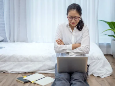 Eine Frau sitzt mit ihrem Laptop auf dem Boden und lernt für den Sprachkurs C1 Französisch