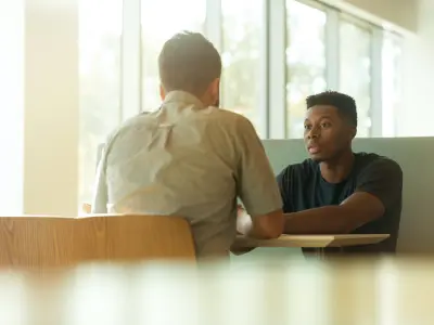 Zwei Männer sitzen an einem Tisch in einer Mensa und unterhalten sich