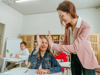 Eine Frau klatscht mit einer Schülerin die an ihrem Platz sitzt ein